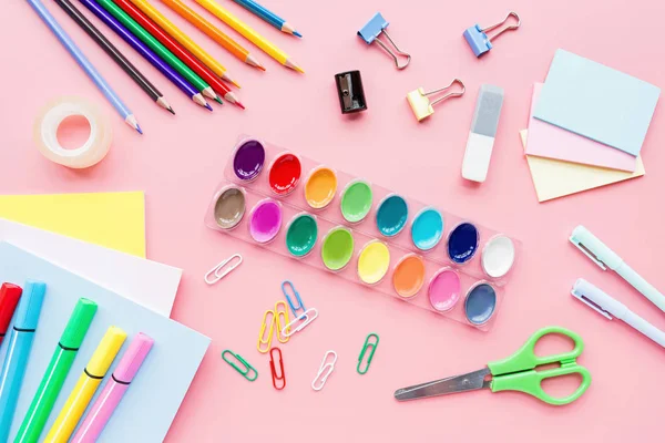 Iskolai kellékek irodaszerek, színes ceruza, festékek, papír rózsaszín háttér, vissza az iskolai koncepció szabad példány hely a szöveg, a modern elemi oktatás. Gyerek asztal, lapos heverő, felülnézet, mockup. — Stock Fotó