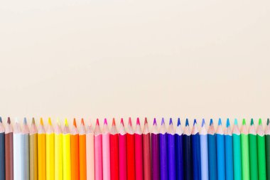 Pastel turuncu kağıt üzerinde yatan birçok boya kalemleri ile parlak ve renkli arka plan. Üst görünüm, düz yatıyordu, mockup, havai, kopyalama alanı. Eğitim ve okul kavramına geri dönüş