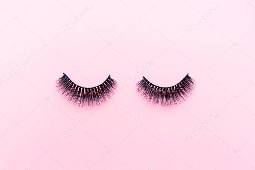 False eyelashes lying on pink background. Beauty and makeup concept. Flatlay, mockup, overhead, top view copy space