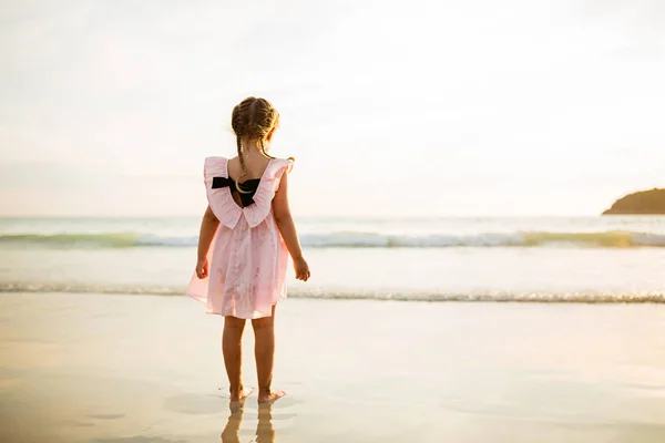 Menina bonito andando na praia. Hora do pôr-do-sol. Criança se divertindo em férias de férias com luz solar de volta - Juventude, estilo de vida, viagem e conceito de felicidade — Fotografia de Stock