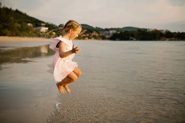Menina bonito pulando na praia. Hora do pôr-do-sol. Criança se divertindo em férias de férias com luz solar de volta - Juventude, estilo de vida, viagem e conceito de felicidade — Fotografia de Stock