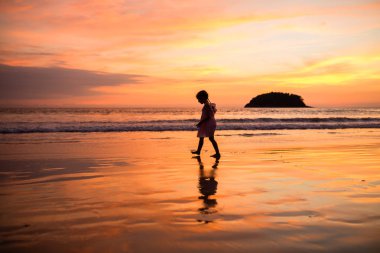 Plajda yürüyen sevimli küçük kız. Gün batımı zamanı. Çocuk arka güneş ışığı ile tatil tatil eğlenmek-gençlik, yaşam tarzı, seyahat ve mutluluk kavramı