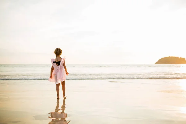 Menina bonito andando na praia. Hora do pôr-do-sol. Criança se divertindo em férias de férias com luz solar de volta - Juventude, estilo de vida, viagem e conceito de felicidade — Fotografia de Stock