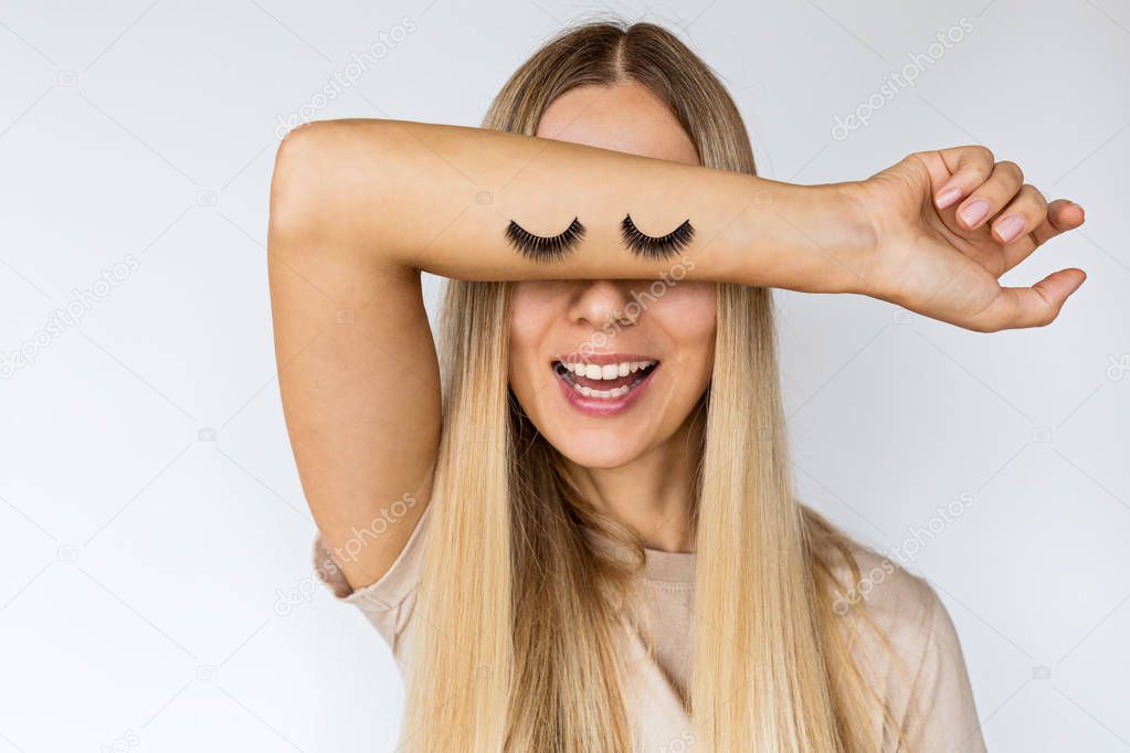 Funny young pretty woman with false eyelashes on her hand. Stylish female covering face with hand on white background. Concept of emotion, beauty, makeup and expression.
