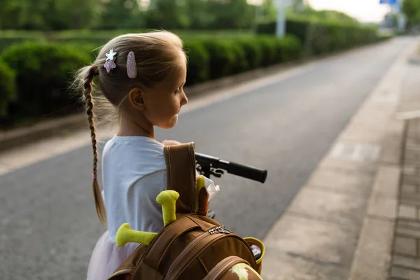 Kid girl pupil from behind walking back to home after learning study school alone with schoolbag, preschool and kindergarten education concept. First day of autumn