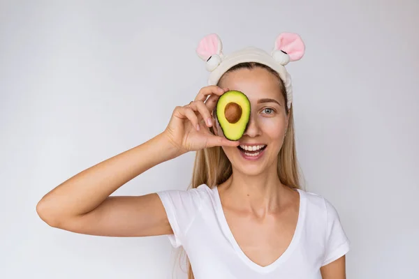 Portret młodej kobiety trzyma rękę świeżego awokado w pobliżu jej twarzy na białym tle. Pielęgnacja skóry i zabiegi spa w domu lub salonie kosmetycznym. Koncepcja Kosmetyka — Zdjęcie stockowe