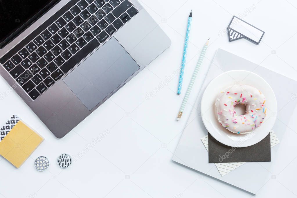 Flat lay, top view office table desk frame. Workspace with laptop, pencil, notebook and donut on white background. Overhead. 