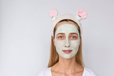 Beyaz arka planda yüzüne doğal avokado maskesi uygulayarak genç bir kadının portresi. Evde veya güzellik salonunda cilt bakımı ve spa uygulamaları. Kozmetoloji konsepti