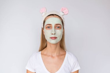 Beyaz arka planda yüzüne doğal avokado maskesi uygulayarak genç bir kadının portresi. Evde veya güzellik salonunda cilt bakımı ve spa uygulamaları. Kozmetoloji konsepti