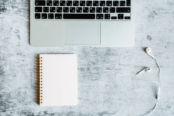 Desktop flatlay: laptop, notebook, headphones lying on gray marble background. Business, finance concept