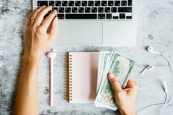 Masaüstü flatlay: dizüstü bilgisayar, Notebook, kadın eller kalem tutarak ve klavyede yazarak, 100 dolar faturaları gri mermer arka planda yatıyor. İş, finans konsepti