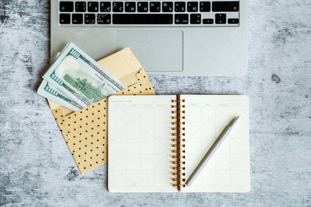 Desktop flatlay: laptop, one hundred dollars bills in envelope lying on gray marble background. Business, finance concept