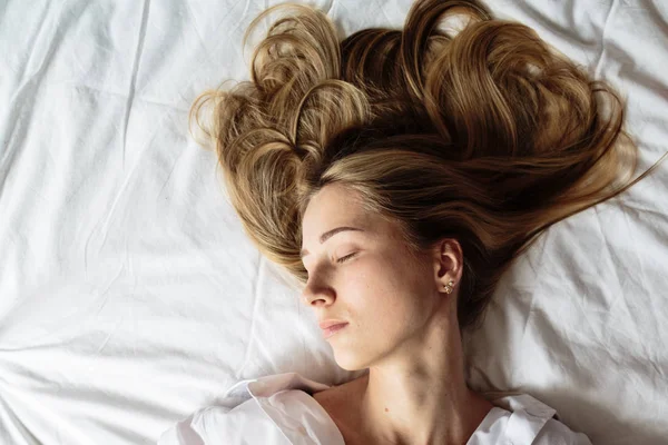 Porträt schöne blonde Frau mit einem schönen Gesicht und erstaunlichen Augen, liegt, schläft auf der Bettwäsche in einem eleganten. und sinnlichen Blicken und kokettiertem Lächeln. Gesundheits- und Harmoniekonzept — Stockfoto