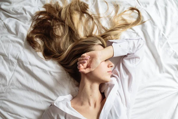 Porträt schöne blonde Frau mit einem schönen Gesicht und erstaunlichen Augen, liegt, schläft auf der Bettwäsche in einem eleganten. und sinnlichen Blicken und kokettiertem Lächeln. Gesundheits- und Harmoniekonzept — Stockfoto