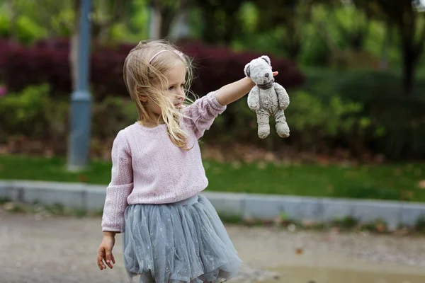 Красива маленька дівчинка в спідниці, що тримає брудний плюшевий ведмідь на відкритому повітрі — стокове фото