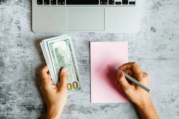 Masaüstü flatlay: laptop, Notebook, kadın elleri gri mermer arka planda nakit yüz dolar faturaları tutarak. İş, finans konsepti
