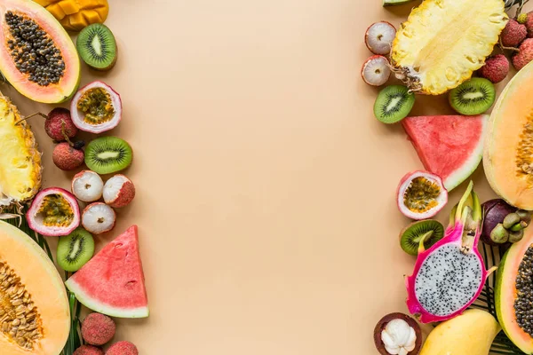 Fresh exotic fruits and tropical palm leaves on pastel orange background - papaya, mango, pineapple, passion fruit, dragon fruit, grapes, lichee, kiwi, melon. Mockup, flat lay, overhead. Top view.