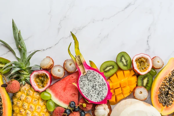 Frutas exóticas frescas y hojas de palma tropical sobre fondo de mármol blanco: papaya, mango, piña, fruta de la pasión, fruta del dragón, melón. Mockup, acostado plano, arriba. Vista superior . — Foto de Stock