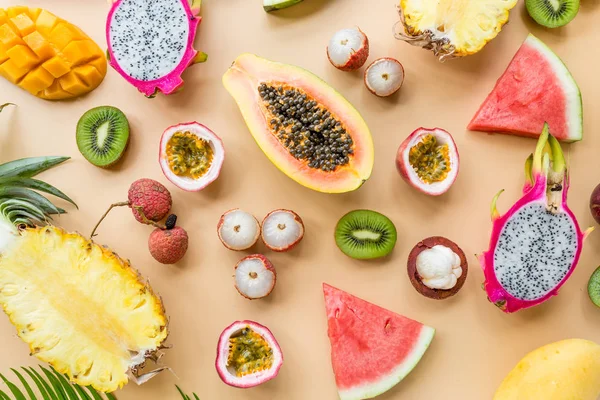 Fresh exotic fruits and tropical palm leaves on pastel orange background - papaya, mango, pineapple, passion fruit, dragon fruit, grapes, lichee, kiwi, melon. Mockup, flat lay, overhead. Top view.