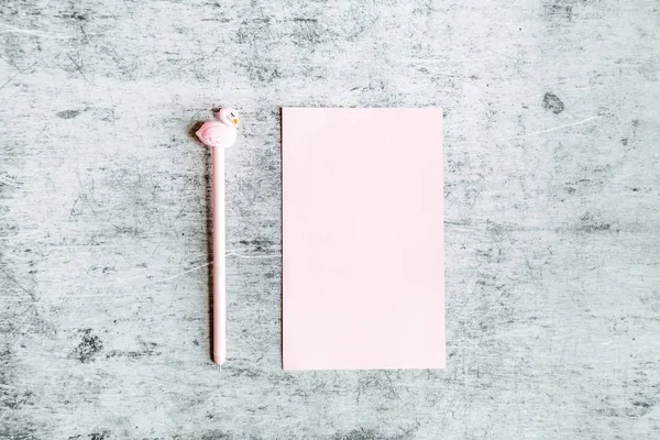 Vista superior maqueta de papel rosa en blanco y bolígrafo con flamenco sobre fondo de hormigón gris. Piso laico, espacio de copia, negocio y concepto de blog. Estilo mínimo — Foto de Stock