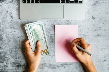 Masaüstü flatlay: laptop, Notebook, kadın elleri gri mermer arka planda nakit yüz dolar faturaları tutarak. İş, finans konsepti