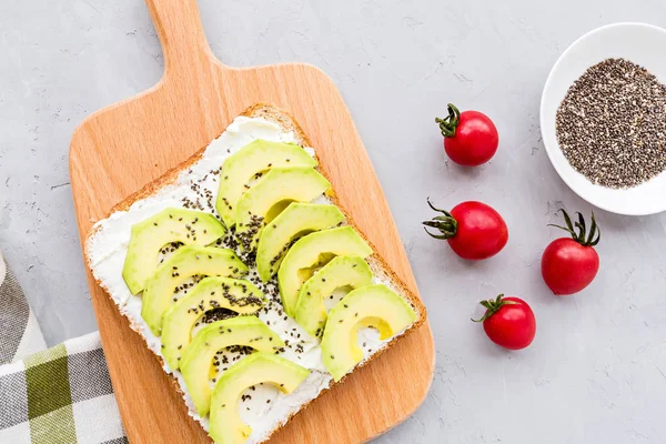 Snacks with avocado. Avocado toast with chia seeds and cream cheese, cherry tomatoes on table. Healthy breakfast lying on gray concrete background. Mockup, flat lay, top view with copy space