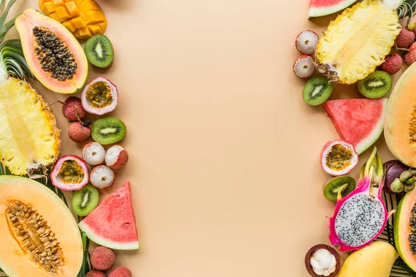 Taze egzotik meyve ve pastel turuncu arka plan tropikal palmiye yaprakları - papaya, mango, ananas, tutku meyve, ejderha meyve, üzüm, lichee, kivi, kavun. Mockup, düz yatıyordu, havai. Üstte görüntü.