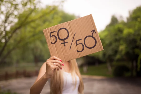 Gender equality concept as woman hands holding a paper sheet with male and female symbol over a crowded city street background. Woman protesting outdoor. Sex sign as a metaphor of social issue.