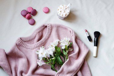 Düz döşeme kompozisyonu. Örme yünlü kazak pembe renk, marshmallow ile kahve fincanı, makarna kurabiye, kozmetik, pastel bej arka plan üzerinde çiçek. Üst görünüm, kopya alanı, mockup. Bahar teması