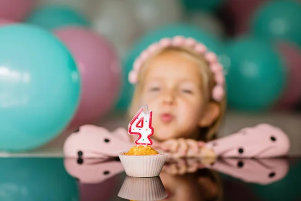 Innenaufnahme eines hübschen fröhlichen kleinen Mädchens mit blonden Haaren, das die Kerze ausbläst, 4 Jahre Geburtstag feiert, modisches Kleid trägt, aufgeregte Mienen hat. Konzept der glücklichen Kindheit — Stockfoto