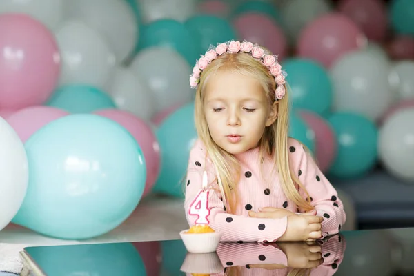 Innenaufnahme eines hübschen fröhlichen kleinen Mädchens mit blonden Haaren, das die Kerze ausbläst, 4 Jahre Geburtstag feiert, modisches Kleid trägt, aufgeregte Mienen hat. Konzept der glücklichen Kindheit — Stockfoto