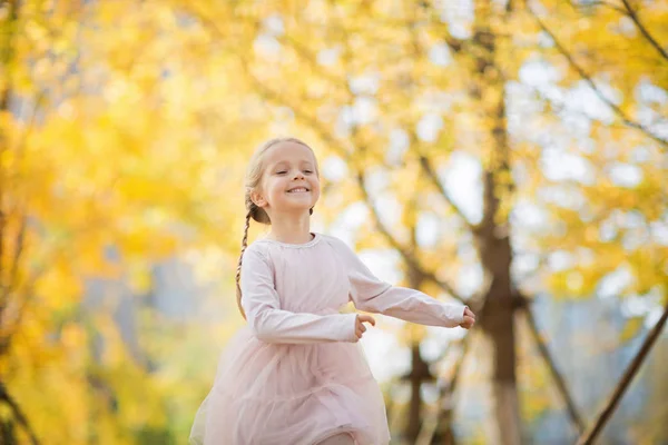 Feliz niña elegante con el pelo largo y rubio corriendo en el parque otoñal con árboles de ginkgo. Temporada de otoño, magia infantil, libertad, concepto de salud — Foto de Stock