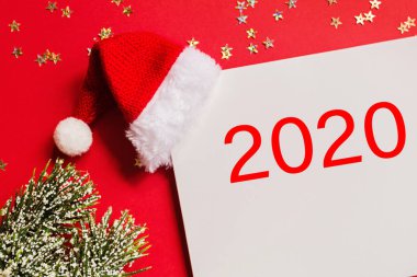 Noel Baba şapkalı boş bir kağıt, hediye, kırmızı arka planda altın konfetili ağaç dalları. Yeni yıl konsepti. Kutlama kartı, xmas kutlaması 2020. Düz konum, şablon, üst görünüm, kopyalama alanı, modelleme