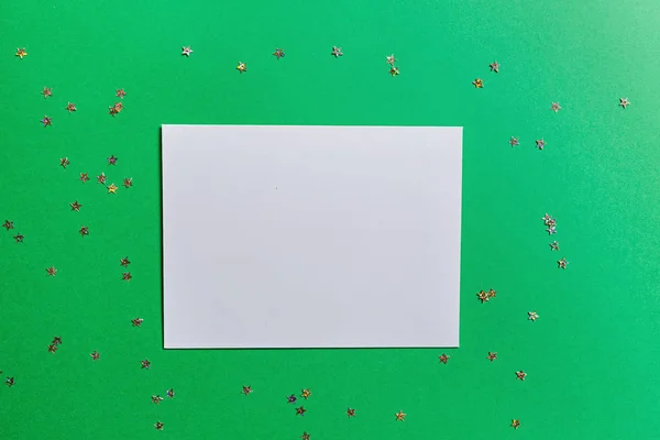 Blanco papier op groene achtergrond met confetti. Nieuwjaarsconcept. Wenskaart, kerstfeest 2020. Platte lay, template, bovenaanzicht, kopieerruimte, mockup — Stockfoto