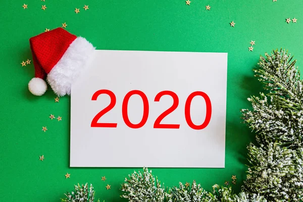 Kosong kertas dengan topi Santa merah, cabang pohon natal dengan latar belakang hijau dengan confetti. Konsep tahun baru. Kartu ucapan, perayaan Natal 2020. Letak datar, templat, tilikan atas, ruang fotokopi, mockup — Stok Foto