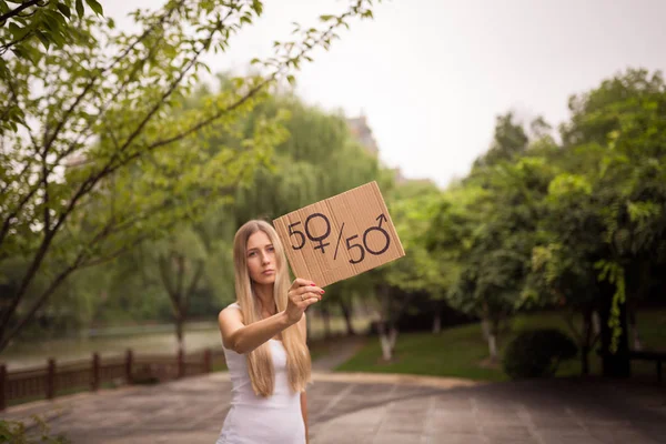 Gender equality concept as woman hands holding a paper sheet with male and female symbol over a crowded city street background. Woman protesting outdoor. Sex sign as a metaphor of social issue.