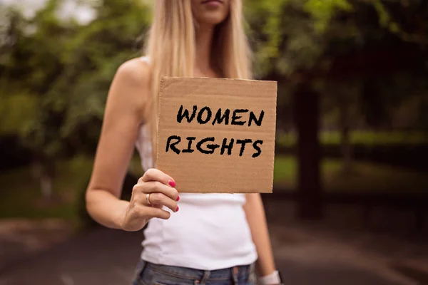 Gender equality concept as woman hands holding a paper sheet with inscription Women rights over a city street background. Woman protesting outdoor. Metaphor of social issue.