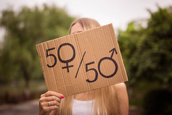 Концепция гендерного равенства как женщины, держащие в руках бумажный лист с мужским и женским символом на переполненном городском фоне. Женщина протестует на улице. Сексуальный знак как метафора социальной проблемы
.