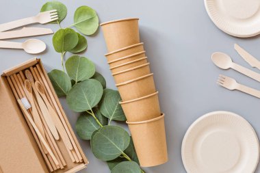 Çevresel doğal kağıt bardaklar, pipetler, tahta çatal bıçaklar gri arka planda yatıyordu. Sürdürülebilir yaşam tarzı kavramı. sıfır atık, plastiksiz eşyalar. Plastik kirliliğini durdurun. Üst görünüm, genel görünüm, şablon, model.