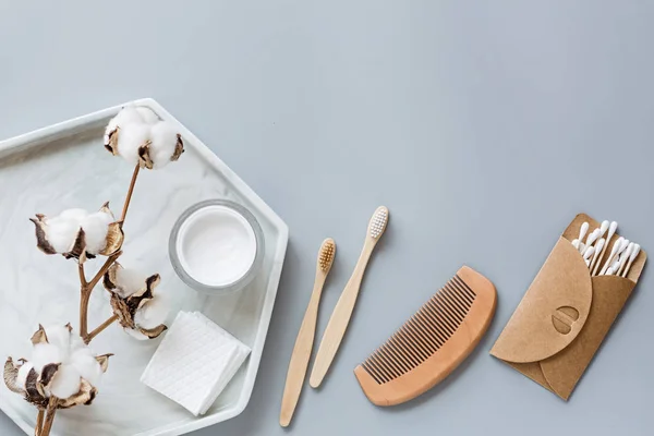 Doğal banyo aksesuarları: ahşap tarak, bambu diş fırçası, yüz kremi, kulak çubuğu, gri kağıtta pamuk çiçeği. Sıfır atık. Model, düz yatak, şablon, üst görünüm, genel giderler