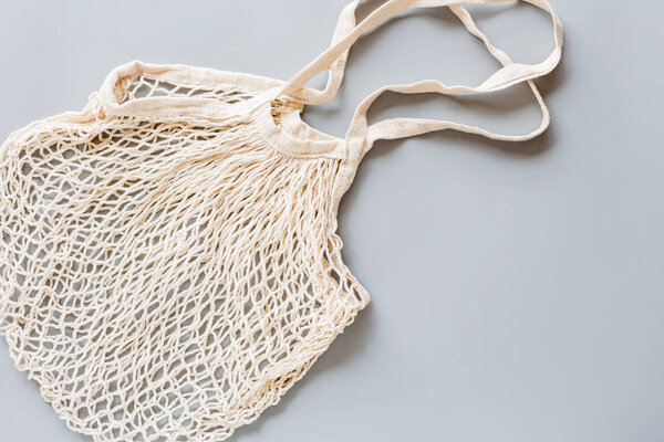 White eco friendly string bag isolated on gray paper background, responsible consumption. Ecological way of life, green and plastic free lifestyle. Flat lay, top view, mockup, overhead, template