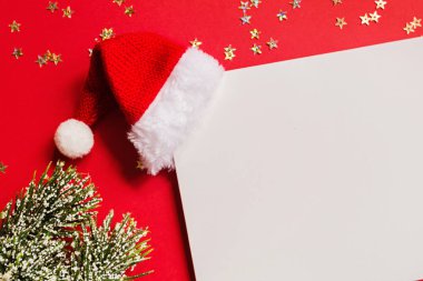 Noel Baba şapkalı boş bir kağıt, hediye, kırmızı arka planda altın konfetili ağaç dalları. Yeni yıl konsepti. Kutlama kartı, xmas kutlaması 2020. Düz konum, şablon, üst görünüm, kopyalama alanı, modelleme