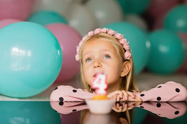 Innenaufnahme eines hübschen fröhlichen kleinen Mädchens mit blonden Haaren, das die Kerze ausbläst, 4 Jahre Geburtstag feiert, modisches Kleid trägt, aufgeregte Mienen hat. Konzept der glücklichen Kindheit — Stockfoto