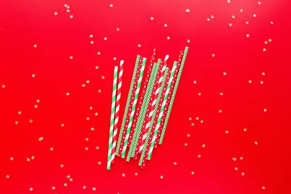 Gestreepte rietjes van verschillende kleuren op rode achtergrond. Nieuwjaar of Kerstmis patroon. Minimalisme concept. Pop art stijl. Bovenaanzicht, Vlakke ligplaats met rietjes voor drinkwater of frisdranken. — Stockfoto