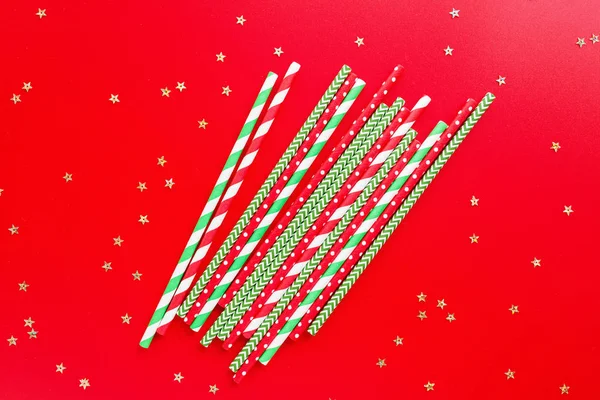Pailles de boissons rayées de différentes couleurs sur fond rouge. Nouvel An ou motif de Noël. Concept de minimalisme. Style pop art. Vue de dessus, Pose plate avec des pailles utilisées pour l'eau potable ou les boissons gazeuses . — Photo
