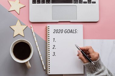Mutlu yıllar 2020. Kadın not defterine 2020 gol attı. Üç renkli arka planda Noel süslemeleri. Üst görünüm, düz görünüm, genel görünüm, kopyalama alanı, model, şablon. Dilekler ve rüyalar konsepti
