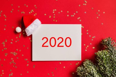 Noel Baba şapkalı boş bir kağıt, hediye, kırmızı arka planda altın konfetili ağaç dalları. Yeni yıl konsepti. Kutlama kartı, xmas kutlaması 2020. Düz konum, şablon, üst görünüm, kopyalama alanı, modelleme