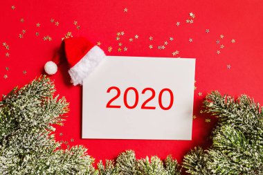 Noel Baba şapkalı boş bir kağıt, hediye, kırmızı arka planda altın konfetili ağaç dalları. Yeni yıl konsepti. Kutlama kartı, xmas kutlaması 2020. Düz konum, şablon, üst görünüm, kopyalama alanı, modelleme