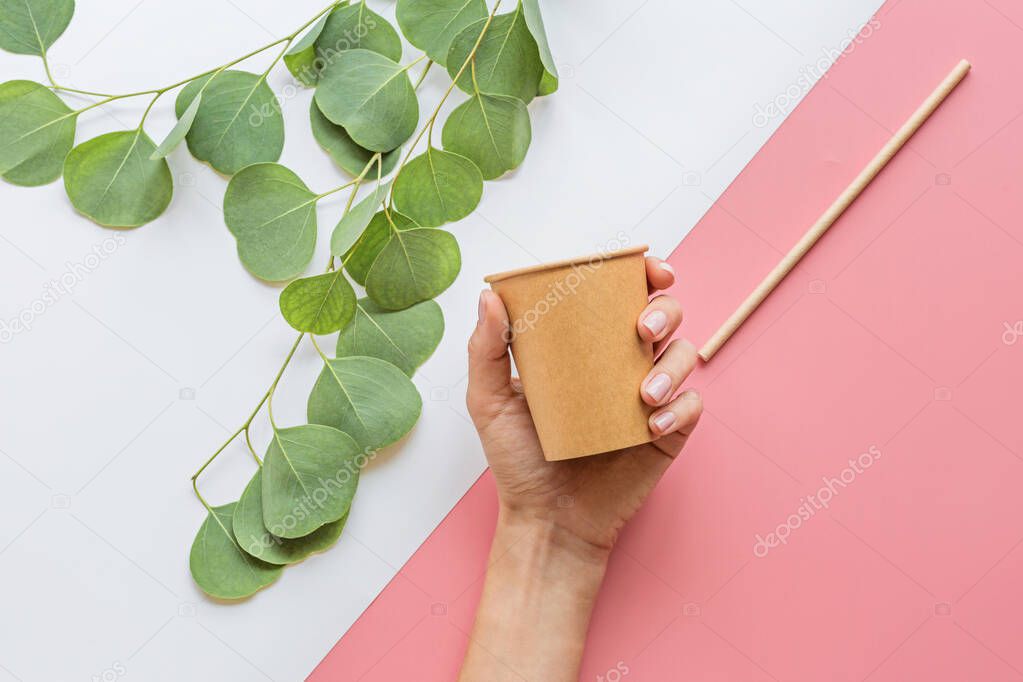 eco natural paper coffee cup, hand and straw flat lay on white and pink background. sustainable lifestyle concept. zero waste, plastic free items. stop plastic pollution. Top view, overhead, mockup
