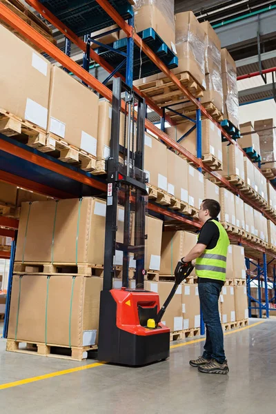 Storehouse medewerker in uniform werken aan vorkheftruck in moderne automatische warehouse.Boxen zijn op de planken van het magazijn. Opslag, machineconcept. Logistiek in stock. — Stockfoto